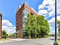Modern condo building showcases red brick, large windows, and vibrant green trees against a blue sky at 715 N Church St # 213, Charlotte, NC 28202