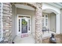 Inviting front porch with stone pillars, a welcome mat, and a decorative wreath on the glass front door at 6021 Piscataway Ct, Rock Hill, SC 29732