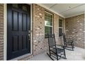 Inviting front porch with rocking chairs, a brick facade, and a black front door at 8514 Ellington Park Dr, Charlotte, NC 28277