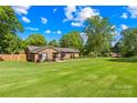 A well-kept brick home on a large green lawn beneath a bright sky and lush trees at 245 Kingsway Cir, Charlotte, NC 28214