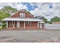 Rear exterior view featuring a brick facade, covered porch, and a fenced yard with paved area at 2036 1St Sw Ave, Hickory, NC 28602