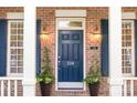 Close-up of a classic blue front door with decorative lanterns and potted plants, framed by brick and white columns at 239 N Faulkner Way, Davidson, NC 28036