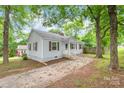 Single-story home with light blue siding, dark shutters, and a quaint front porch nestled among mature trees at 104 Willetta Dr, Charlotte, NC 28217