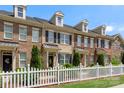 Attractive brick townhome displaying dormers, black shutters, landscaping, and a white picket fence at 4313 Courtly Ln, Belmont, NC 28012