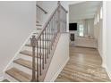 Elegant staircase with hardwood treads and decorative iron railing leads to a naturally lit living area at 18026 Stark Way, Charlotte, NC 28278