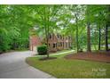 Brick home exterior with a sprawling lawn, mature trees, and a curved driveway and attached garage at 8227 Lansford Rd, Charlotte, NC 28277