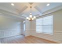 Dining room featuring elegant wainscoting, tray ceiling with chandelier, and wood-look flooring at 3022 Burnello Ct, Iron Station, NC 28080