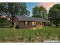 Charming single-story brick home with mature trees and a spacious front yard at sunset at 804 Gw Broome Rd, Monroe, NC 28112