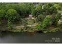 Aerial view of a home with lush landscaping, a detached garage, and serene pond views at 5100 Crestland Ave, Charlotte, NC 28269
