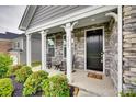 Inviting front porch featuring stone accents, black front door, and charming rocking chairs at 7049 Irongate Dr, Indian Land, SC 29707