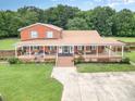 A beautiful aerial view of a two-story red brick home, lush green lawn, and wrap around porch at 907 Sikes Mill Rd, Monroe, NC 28110