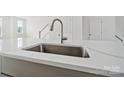 Close-up of a kitchen sink with a modern faucet, white countertop, and view of the staircase at 2134 Barrowcliffe Nw Dr # 0006, Concord, NC 28027