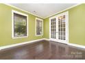 Bright room featuring hardwood floors, green walls, white trim, two windows with blinds, and glass french doors at 15536 Oleander Dr # L228, Charlotte, NC 28278