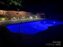 Tranquil backyard pool illuminated at night, surrounded by landscape lighting and a wooden fence for privacy at 3320 Harvey Ln, Monroe, NC 28110