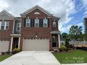 A charming brick townhome featuring a two-car garage and classic architectural details under a cloudy sky at 12047 Lavinia Ln, Charlotte, NC 28277