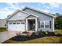 Charming gray home featuring a two-car garage, stone accents, manicured lawn and covered front porch entrance at 107 S Sina St, Troutman, NC 28166