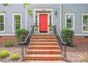 Inviting entryway with brick steps, a red door, manicured bushes, and decorative wall lanterns at 10338 Hollybrook Dr, Charlotte, NC 28277