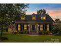 Charming brick home at dusk featuring a landscaped front yard and dormer windows at 1208 Chausley Ct, Charlotte, NC 28211