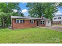 Landscaped yard featuring a charming brick home, dark shutters, and a paved driveway at 2401 Woodleaf Dr, Gastonia, NC 28052