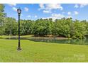 Picturesque pond view with lush green grass, mature trees, and a classic lamp post adding to the serene setting at 9831 Sedgefield Dr, Waxhaw, NC 28173