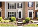 A townhome exterior with a welcoming black door, flanked by well-manicured shrubs and complemented by dark shutters at 15623 Sir Charles Pl, Charlotte, NC 28277