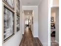 Inviting hallway featuring wood flooring, elegant artwork, crown molding, and views into the living spaces and bedroom at 1600 Baymont Ct, Stanley, NC 28164