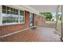 Charming covered front porch boasts red tile flooring, brick detail, black security door, and white railing at 800 Old Little Rock Rd, Charlotte, NC 28214
