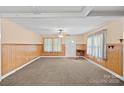 Spacious living room with neutral carpet, wood paneled walls, ceiling fan, and natural light at 1000 Peachtree Rd, Charlotte, NC 28216
