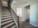 Staircase with dark wood and metal railing leading to a view of the kitchen with white cabinets at 4131 Black Ct # 170, Harrisburg, NC 28075