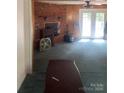 Living room with a brick fireplace, wood paneling, carpeted floors, and access to outdoor french doors at 8524 Anette Ave, Mint Hill, NC 28227
