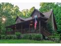 Log cabin home with a covered front porch, lush landscaping, steps, and an American flag at 95 Odell Ct, Taylorsville, NC 28681