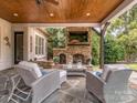 Comfortable outdoor seating area with a stone fireplace and ceiling fan on a covered patio with a stone floor at 1404 Lookout Cir, Waxhaw, NC 28173