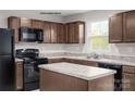 A kitchen with a center island, brown cabinets, stainless steel sink, and black appliances at 336 Maplestead St # 1080, Lancaster, SC 29720