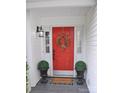 Close-up of a vibrant red front door with a decorative wreath, flanked by potted topiaries on a covered porch at 1051 Streamlet Way, Monroe, NC 28110