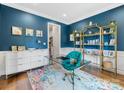 Home office with blue walls, a glass desk, gold shelving, and colorful decor at 15313 Moate Ct, Huntersville, NC 28078