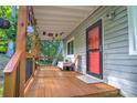 Inviting covered porch featuring wood decking, railing, seating, and a vibrant red front door at 5995 Tall Tree Ln, Harrisburg, NC 28075