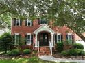 Traditional red brick home with a covered entrance, an American flag, and established shrubs at 8612 Tintinhull Ln, Waxhaw, NC 28173