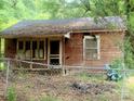 Exterior view of a small home featuring weathered siding, surrounded by overgrown trees and a chainlink fence at 711 East Dr, Cherryville, NC 28021