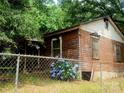 A small home featuring weathered siding, surrounded by overgrown trees and a chainlink fence at 711 East Dr, Cherryville, NC 28021