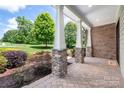 Covered porch featuring stone columns, brick flooring, and landscaped garden views at 1500 Tarrington Way, Wesley Chapel, NC 28079