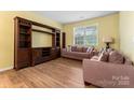 Spacious living room with wood-look flooring, a large entertainment center, and comfortable seating by a bright window at 1911 Savannah Hills Dr, Matthews, NC 28105