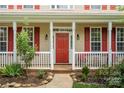 Inviting front porch with a red front door, white columns and railings, framed by lush landscaping at 6614 Truman St, Indian Trail, NC 28079