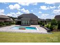 Backyard view of a refreshing swimming pool with a stone waterfall feature and a spacious patio area at 720 Cavesson Way, Monroe, NC 28110