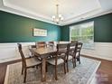 Elegant dining room features rich green walls, wainscoting, a modern chandelier, and a large window at 9507 Reid Hall Ln, Matthews, NC 28105