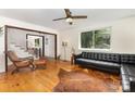 Bright living room featuring hardwood floors, staircase, ceiling fan and comfortable black leather sofa at 7015 Lavern St, Charlotte, NC 28215