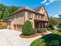 A stunning view of a brick house showcasing a three-car garage, manicured landscaping, and a curved walkway at 13056 Long Common Pkwy, Huntersville, NC 28078
