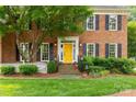 A sunny yellow front door welcomes visitors to this brick home with black shutters and meticulously manicured landscaping at 5517 Alexa Rd, Charlotte, NC 28277