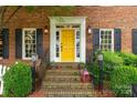 Inviting front porch with yellow door, brick steps, decorative lanterns, lush greenery, and a warm, welcoming ambiance at 5517 Alexa Rd, Charlotte, NC 28277