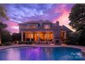 A luxurious backyard with a serene pool, covered patio, and brick fireplace against a dramatic evening sky at 1509 Churchill Downs Dr, Waxhaw, NC 28173