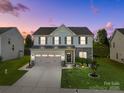Charming two-story home at dusk featuring a well-manicured lawn and attached two-car garage at 1725 Mill Creek Sw Ln, Concord, NC 28025